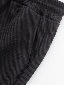 Detailed view of the textured waffle fabric and side pocket on dark casual straight-leg pants