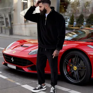 Male model in black corduroy half-zip tracksuit standing next to a luxury red car