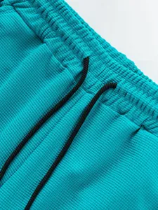 Close-up of turquoise waffle knit pants featuring elastic waistband and black drawstring.
