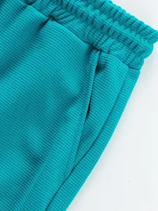 Close-up detail of teal ribbed fabric pants showing waistband and side pocket texture