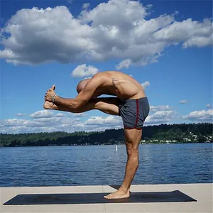 Fitte man in grijze sneldrogende sportshort rekt op een yogamat bij een prachtig meer