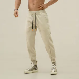 Detail of men's slim fit joggers with tapered cuffs and side zipper pockets in beige.