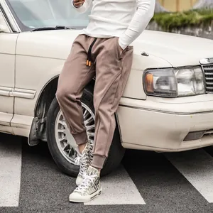 Detail of men's brown joggers featuring orange drawstring tips and secure zipper pockets.
