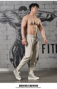 Men's beige loose sports joggers featuring a drawstring waist in a modern gym setting