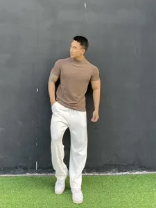 Male model wearing brown short-sleeve mock neck gym t-shirt with white casual pants
