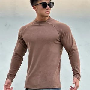 Man in a brown slim fit muscular long sleeve crew neck fleece base layer shirt against a wall