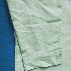Close-up detail of cuff and button on light green cotton linen long sleeve shirt