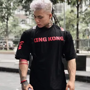 Modelo con camiseta deportiva negra holgada y estampado rojo de King Kong en exterior.