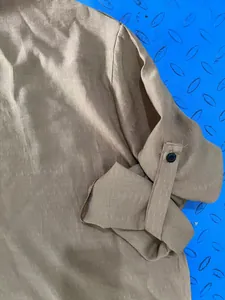 Close-up detail of the roll-up sleeve tab and button on a men's brown linen shirt