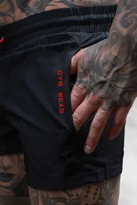 Close-up of black gym shorts featuring red GYM WEAR text on the side pocket
