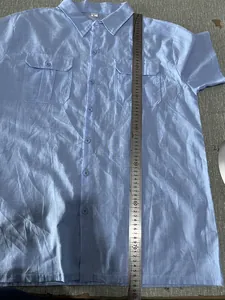 Measurement detail showing the length of a light blue cotton linen shirt with a ruler