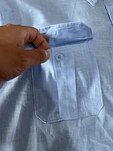 Close-up detail of the buttoned flap pocket on a light blue men's linen cotton shirt