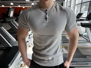 Close-up detail of a grey ribbed muscle fit Henley t-shirt worn by a model in a gym