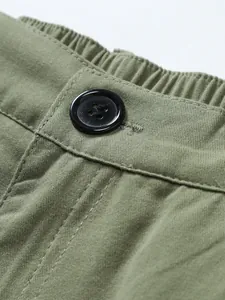 Macro detail of army green woven men's shorts featuring a black button and elastic waist