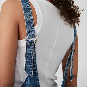 Detailed close-up of adjustable shoulder straps with metal D-rings on blue denim overalls.