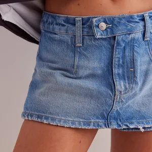 Detailopname van een blauwe denim skort met een metalen knoop en een gerafelde zoom.