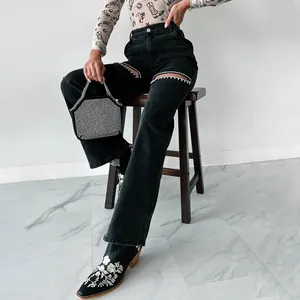 Detailed shot showing the sparkling rhinestone trim on black ripped straight-leg jeans