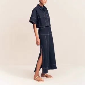 Detail of dark indigo denim two-piece set featuring contrast white stitching and a split maxi skirt