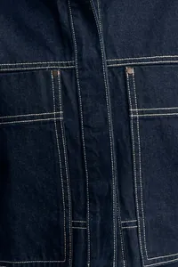 Close-up detail of dark blue denim shirt with contrast stitching and pocket rivets