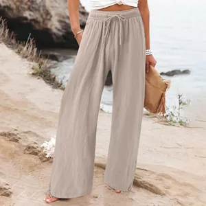 Close-up detail of women's beige wide-leg trousers with drawstring elastic waist on a beach