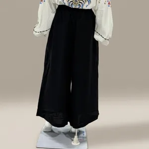 Back view of loose black wide-leg trousers on a mannequin in a storage warehouse