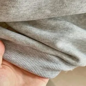 Dettaglio macro del tessuto grigio della felpa che mostra la texture morbida e il polsino.