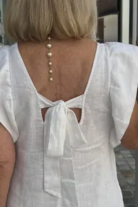 Detailed view of a white linen dress back featuring an elegant bow tie and flutter sleeves.