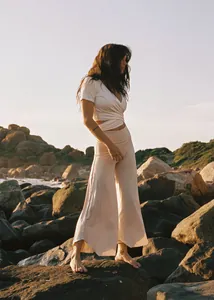 Woman wearing a beige wrap top and high waist wide leg yoga pants on a rocky beach