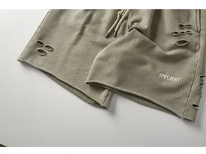 Close-up detail of men's distressed cargo shorts in olive green with SPRCJEOT embroidery