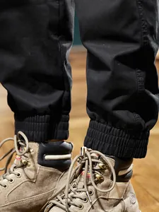 Gros plan de pantalon cargo noir à chevilles élastiques avec bottes de travail brunes.