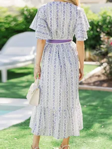 Back view of elegant bohemian floral ruffle maxi dress with purple belt in a sunny garden setting