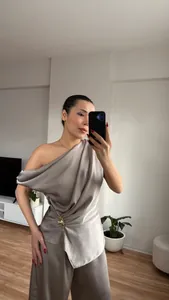 Nahaufnahme des eleganten Faltenwurfs des grauen One-Shoulder-Satin-Tops mit Hose
