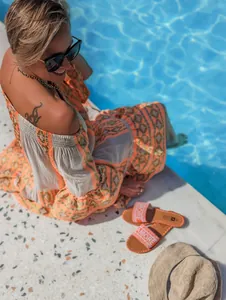 Detail view of a bohemian off-shoulder tiered midi dress with orange patterns by a pool