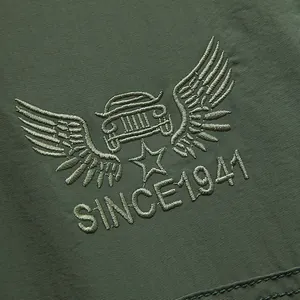 Close-up of olive green outdoor pants featuring embroidered winged car logo and SINCE 1941