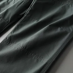 Detailed close-up showing durable double stitching on dark green tactical outdoor pants.