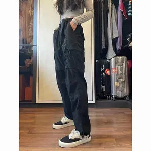 Full length side view of women's black waterproof techwear cargo pants in room.
