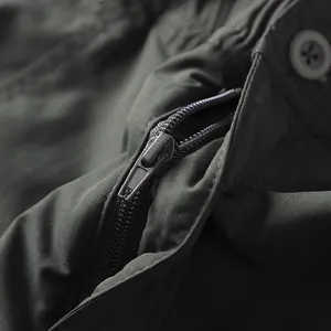 Dettaglio ravvicinato della cerniera metallica su un pantalone da trekking verde.