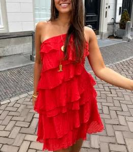 Detail van een levendige rode mini-jurk met ruches en één schouder in een zonnige straat