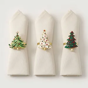 Detail showing three unique alloy Christmas tree napkin rings on folded beige napkins.