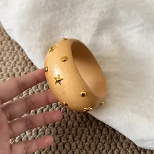 Detailaufnahme eines breiten Armreifs im Holzstil mit goldenen Sternen und Nieten.