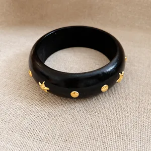 Vintage schwarzer Armreif mit goldenen Stern- und Punktnieten auf beigem Stoffhintergrund