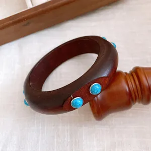 Nahaufnahme eines Vintage Holzarmreif mit türkisfarbenen Steinen auf einem Holzständer