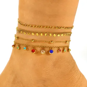 Close-up of layered gold stainless steel anklets with colorful crystal stone charms.