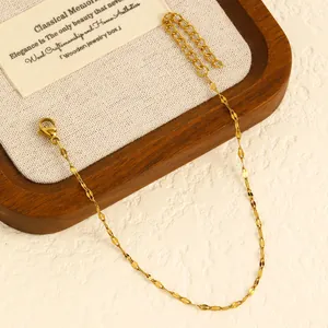 Close-up detail of a delicate gold-plated stainless steel chain anklet on a wooden tray