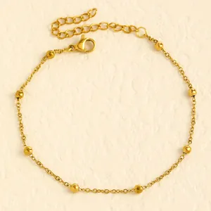 Detailed view of a gold stainless steel beaded anklet on a textured stone surface.