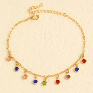 Detailed view of gold stainless steel anklet with colorful charms on a beige background