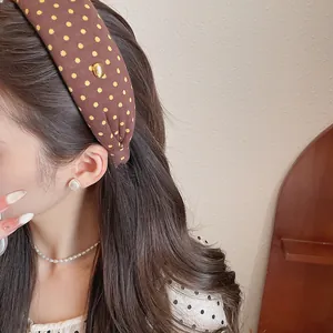 Elegant brown polka dot fabric wide headband worn by model in a soft warm setting