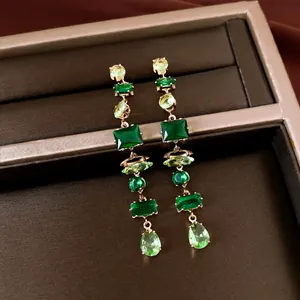 Detalle de pendientes largos de circón verde esmeralda con formas cuadradas y pera