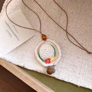 Detailed view of a handmade crochet hat pendant necklace with an acorn charm and flowers.