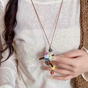 Close-up of a pastoral flower basket pendant necklace with colorful beads and leather cord.